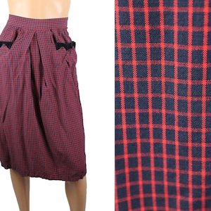 May include: A red and black plaid skirt with black bow accents on the pockets. The skirt is knee-length and has a pleated design.