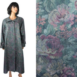 May include: A long, full-length coat featuring a dark teal and muted purple floral tapestry pattern. The garment has a wide collar, long sleeves with cuffs, and a button-front closure. The fabric displays a dense, woven texture with roses.