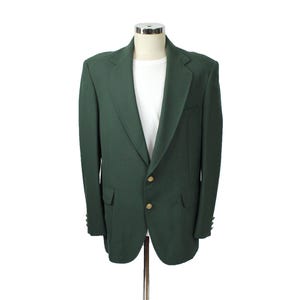 May include: A dark green blazer with gold-colored buttons and a white undershirt. The blazer is displayed on a mannequin against a white background. The blazer has a classic design with a notched lapel and two front pockets.