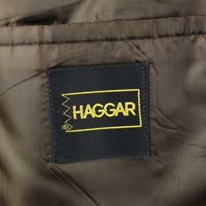 Op de afbeelding: Een zwart label met gouden stiksels en het woord "HAGGAR" in gouden letters.