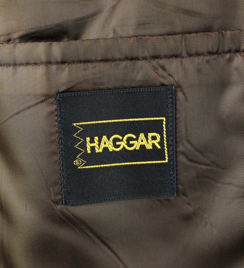 Op de afbeelding: Een zwart label met gouden stiksels en het woord "HAGGAR" in gouden letters.