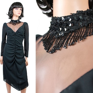 May include: A black dress with a sheer neckline and a beaded and sequined collar. The dress has a gathered bodice and a flowing skirt.