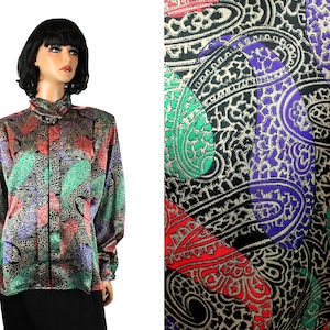 Puede incluir: Una blusa de manga larga con estampado paisley en tonos rojos, verdes, negros y dorados. La tela tiene un acabado satinado.