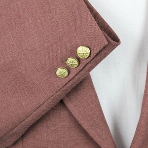 May include: Close-up of the sleeve of a maroon blazer with four gold buttons. Each button has a decorative design.