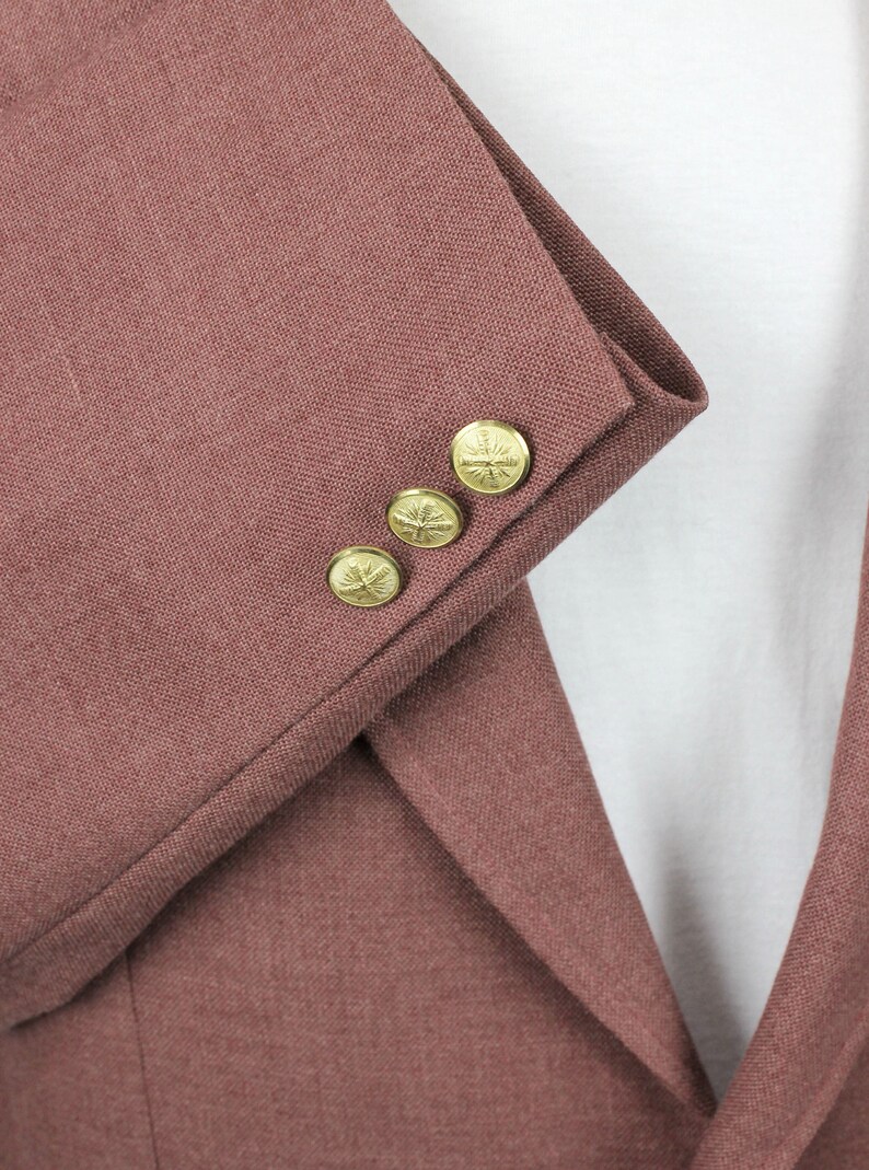 May include: Close-up of the sleeve of a maroon blazer with four gold buttons. Each button has a decorative design.