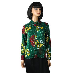 Può includere: Camicia verde a maniche lunghe con motivo floreale. La camicia presenta un motivo di fiori gialli, rossi e bianchi. I polsini sono rossi. La camicia è indossata con una gonna nera. Colletto button-down.