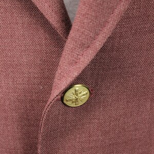 May include: A close-up of a burgundy blazer with a gold button featuring a stylised leaf design.