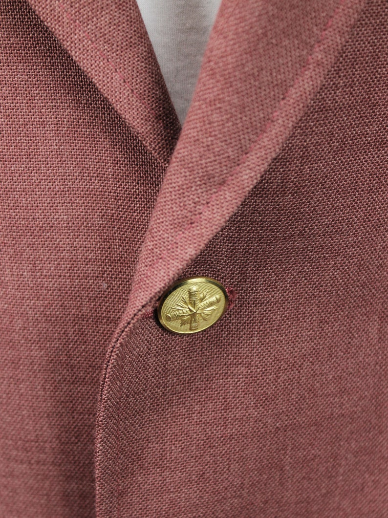 May include: A close-up of a burgundy blazer with a gold button featuring a stylised leaf design.