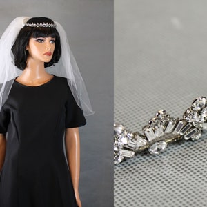 May include: A white bridal veil with a silver tiara featuring clear rhinestones. The veil is made of tulle and has a scalloped edge.