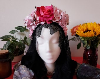 May include: A pink and white flower crown with black lace veil. The crown is made of silk flowers and is worn on a white mannequin head.