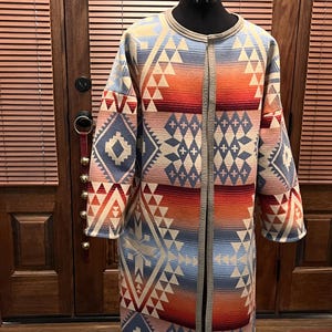 May include: A long, patterned cardigan with a geometric design in shades of blue, red, orange, and white. The cardigan has a shawl collar and a front closure.