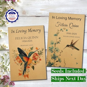 May include: Two rectangular tan paper packets labelled In Loving Memory for Felicia Quinn 1950-2025 Wildflower seeds. One packet features a colourful hummingbird with orange and green flowers, the other a blue floral stem and a flying hummingbird.