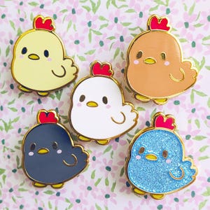 以下が含まれることがあります： 漫画のニワトリの形をした5つのエナメルピン。各ピンには金の縁と赤い鶏冠があります。ニワトリは黄色、茶色、白、ネイビーブルー、キラキラ光る青色です。