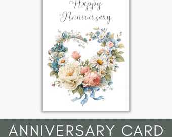 May include: A white anniversary card featuring the text Happy Anniversary in elegant script. Below the text is a heart-shaped floral arrangement composed of white, pink, and blue flowers, green leaves, and a light blue ribbon tied at the bottom.