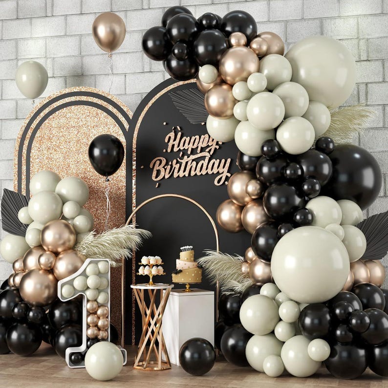 May include: A black, gold, and cream balloon arch with the words "Happy Birthday" in gold letters. The arch is decorated with a number one balloon made of smaller balloons.