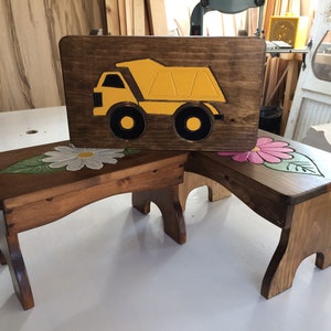 May include: Three wooden children's stools with painted designs. One stool has a yellow dumper truck, one has a white daisy, and one has a pink flower.