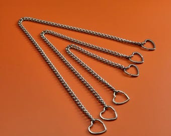 Può includere: Catene in metallo argentato con ciondoli a forma di cuore. Le catene sono disposte diagonalmente su uno sfondo arancione. Ogni catena ha un piccolo ciondolo a forma di cuore alla fine. Le catene sono fatte di piccoli anelli interconnessi.