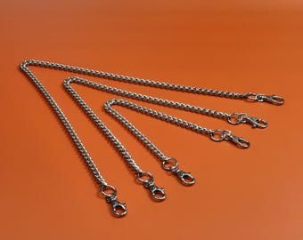 Può includere: Catene in metallo color argento con chiusure a moschettone di diverse lunghezze, disposte diagonalmente su uno sfondo arancione. Queste catene sono probabilmente per una borsa o un altro accessorio.