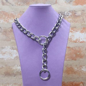 May include: A silver-toned metal chain necklace featuring a Y-shaped design. The necklace consists of thick, interlocking oval links that connect to a central circular ring, with a shorter vertical chain segment ending in a second circular ring.