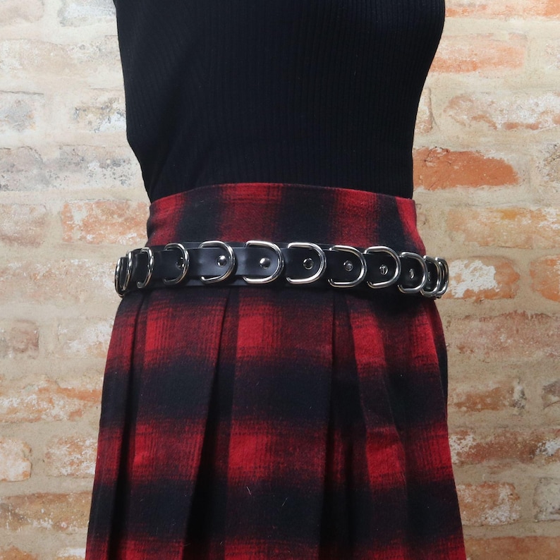 Angled view of The Havoc Belt on a mannequin, welded D-rings and black leather over a red tartan pleated skirt