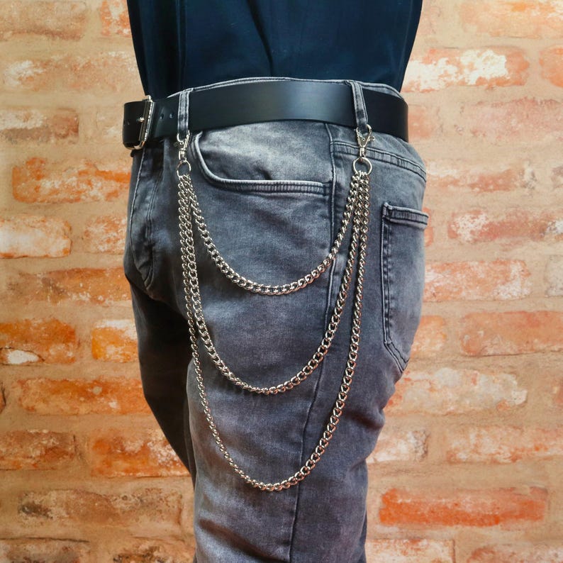 Pu&ograve; includere: Accessorio con catena in metallo argentato attaccato a una cintura nera e jeans grigi. La catena &egrave; appesa in tre fili paralleli. La cintura ha una fibbia argentata. I jeans hanno un classico design a cinque tasche.