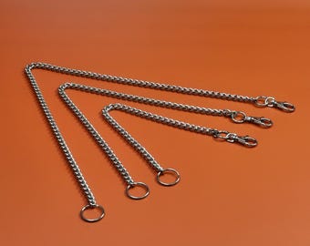 Può includere: Quattro catene metalliche color argento di diverse lunghezze. Ogni catena ha un piccolo anello a un'estremità e un moschettone all'altra. Le catene sono disposte su uno sfondo arancione.