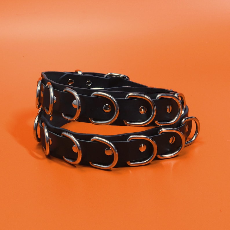 The Havoc Belt - wide black leather belt coiled in two rows showing the line of welded nickel D-rings and rivets