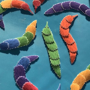 May include: A collection of colorful, fuzzy, worm-like creatures with segmented bodies. The worms are arranged in a variety of positions on a blue background.