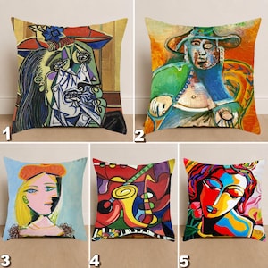 May include: Five decorative throw cushions featuring abstract art in the style of Picasso. Each cushion displays a different colourful painting, including portraits and musical instrument themes. The cushions are square and appear to be made of a soft fabric.