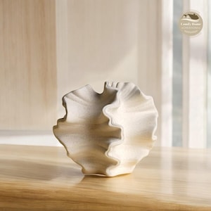 Peut inclure: Un vase en céramique blanche avec un design unique et plissé. Le vase est fait d'un matériau texturé et a une forme ronde et lisse.