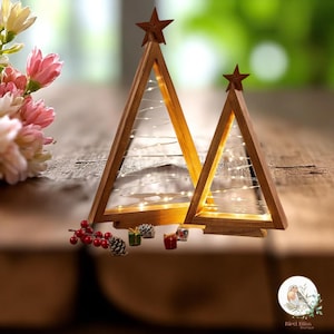 Könnte beinhalten: Zwei Weihnachtsbaumdekorationen aus Holz mit Sternaufsätzen und Lichterketten. Die Bäume sind unterschiedlich groß und stehen auf einer Holzoberfläche. Kleine dekorative Geschenke und Tannenzapfen befinden sich an der Basis der Bäume.