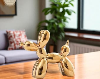 May include: A golden balloon dog sculpture with a glossy finish. The dog is posed in a playful stance, with its head and tail raised. The sculpture is placed on a wooden table, with a blurred background of a living room.