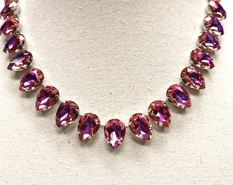 May include: A silver necklace with a row of teardrop-shaped pink and purple crystals.