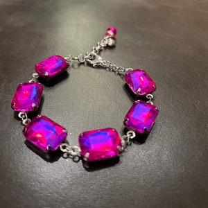 May include: A silver bracelet with six large, rectangular, iridescent pink gemstones. The bracelet has a lobster claw clasp.