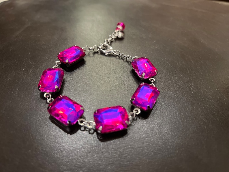 May include: A silver bracelet with six large, rectangular, iridescent pink gemstones. The bracelet has a lobster claw clasp.