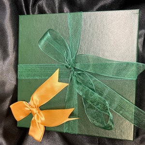 May include: A green gift box with a gold ribbon and a green bow. The box is wrapped in a green paper with a subtle texture.
