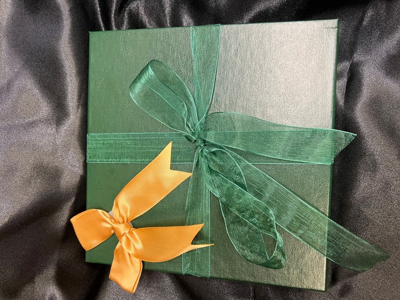 May include: A green gift box with a gold ribbon and a green bow. The box is wrapped in a green paper with a subtle texture.