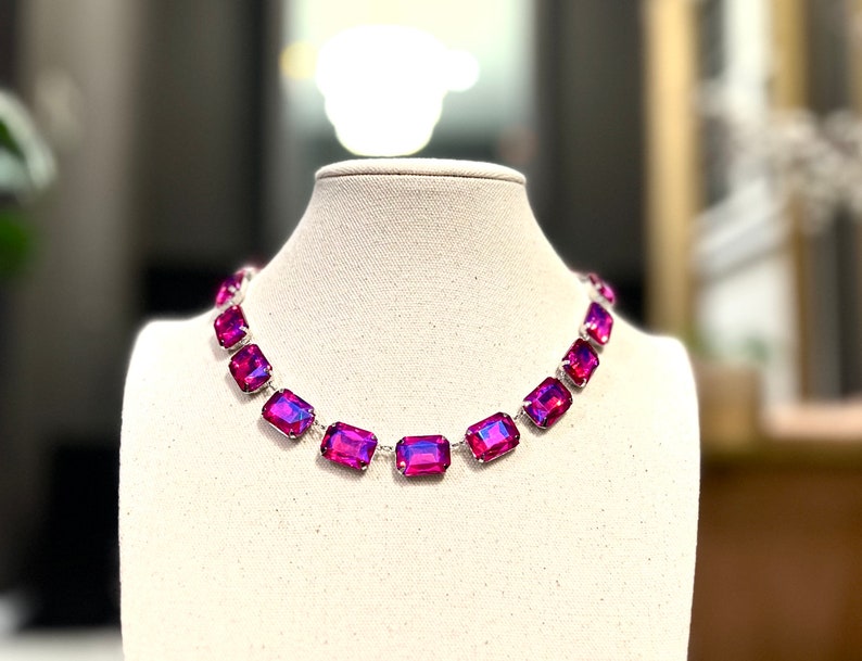 May include: A silver chain necklace with a row of large, rectangular, iridescent pink gemstones.