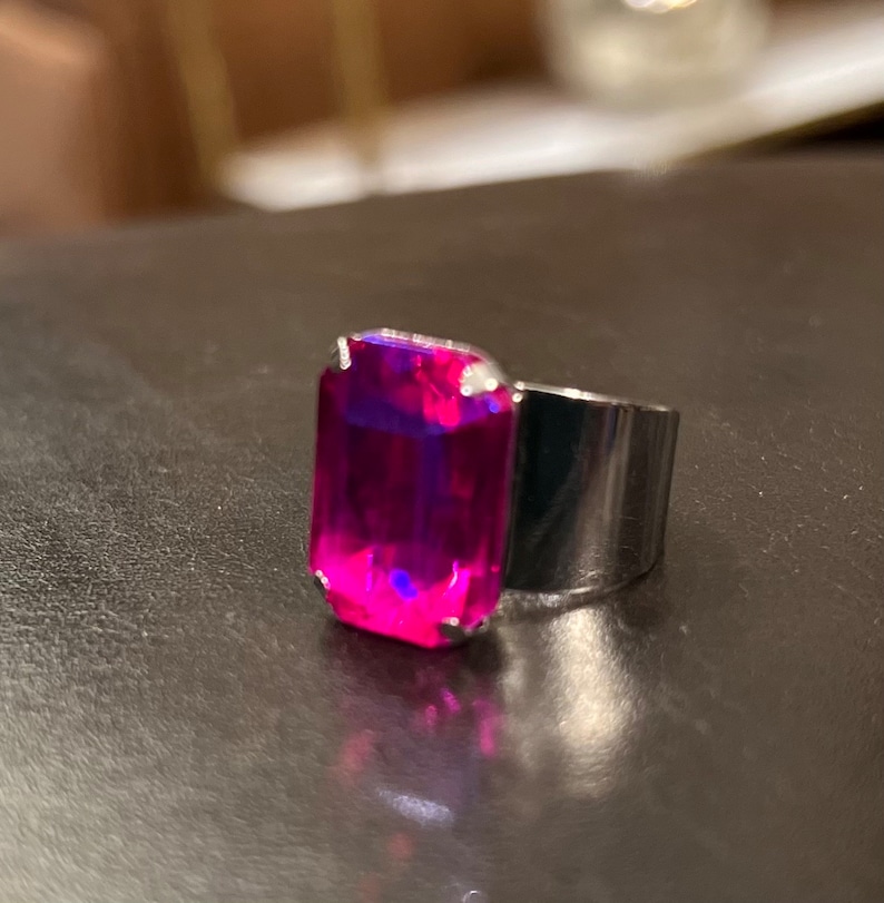 May include: A silver ring with a large, bright pink, emerald-cut gemstone.