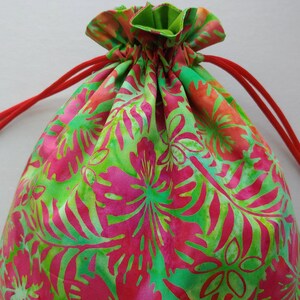 May include: A drawstring bag with a vibrant floral pattern in shades of pink, green, and orange. The bag features a red drawstring closure and a green interior lining. The fabric is patterned with large stylized flowers and leaves.