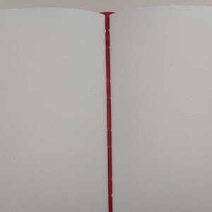 May include: Open notebook with blank white pages and a red spine. The pages are clean and ready for writing or drawing. The binding is a vibrant red, providing a striking contrast to the white pages.