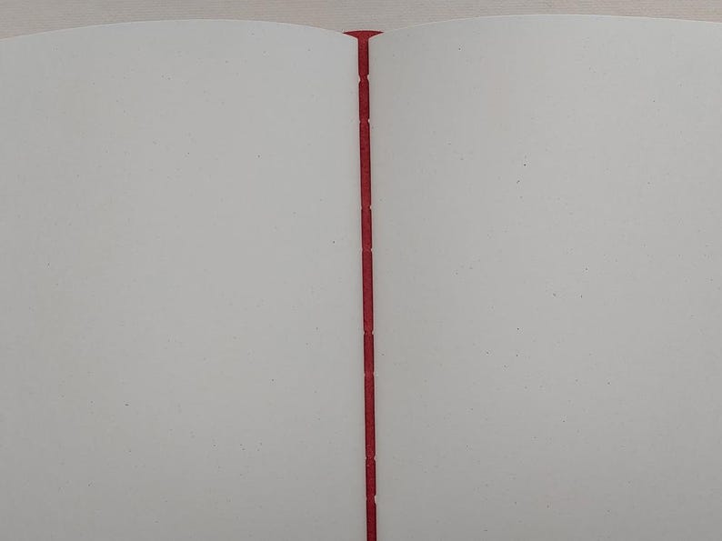 May include: Open notebook with blank white pages and a red spine. The pages are clean and ready for writing or drawing. The binding is a vibrant red, providing a striking contrast to the white pages.