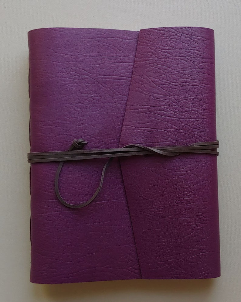 Puede incluir: Un diario encuadernado en cuero morado con una correa de cuero marr&oacute;n y cierre de nudo.