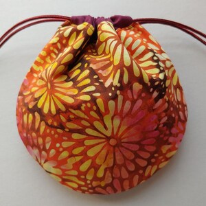 May include: A drawstring bag made of fabric with a colorful floral pattern in shades of orange, yellow, and pink. The bag has a maroon drawstring.