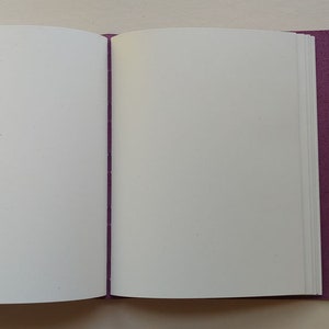 Puede incluir: Un diario encuadernado en cuero morado con p&aacute;ginas en blanco, abierto para revelar el papel blanco en el interior.