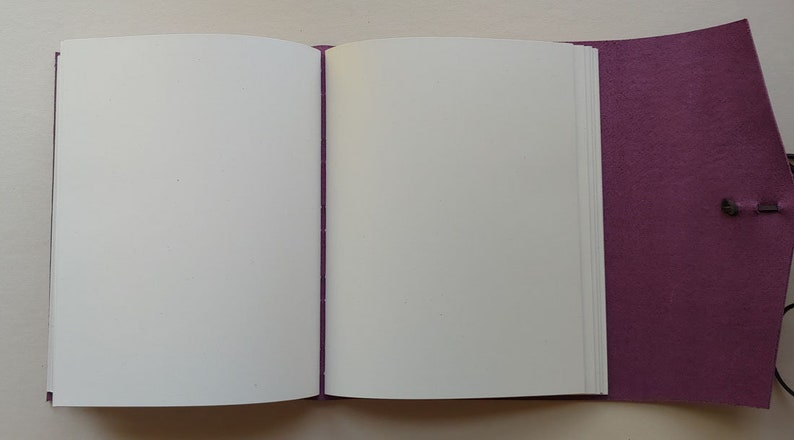 Puede incluir: Un diario encuadernado en cuero morado con p&aacute;ginas en blanco, abierto para revelar el papel blanco en el interior.