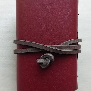 May include: A small burgundy leather journal with a brown leather strap and knot closure.