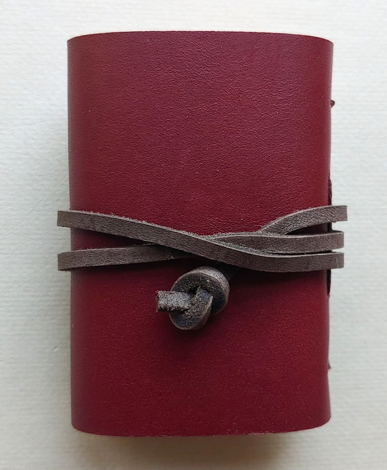 May include: A small burgundy leather journal with a brown leather strap and knot closure.