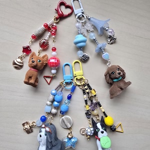 May include: Four handmade keychains with dog figurines. Each keychain features a different dog breed, adorned with colorful beads, charms, and a metal clasp. The keychains include a baseball charm, stars, and a heart-shaped clasp.