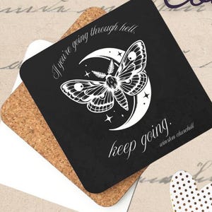 May include: A set of cork-backed coasters. One black square coaster features a moth and moon design with the quote "If you're going through hell, keep going." A white and cork coaster are also visible.